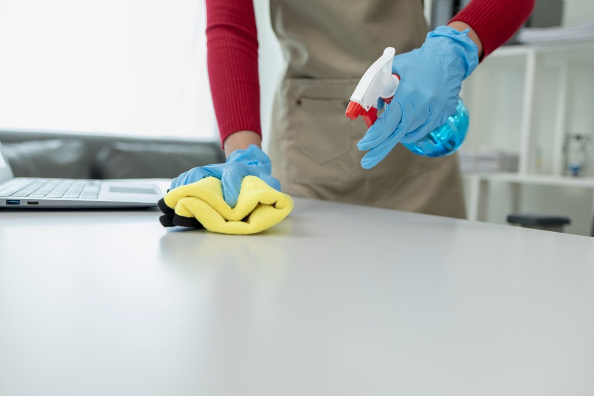 Cleaning desk surface in office with sanitizer spray, wear glove Declutter Before You Clean