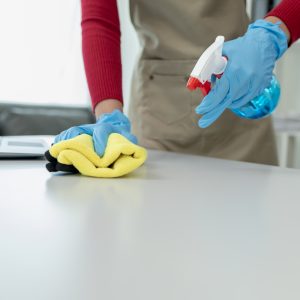 Cleaning desk surface in office with sanitizer spray, wear glove Declutter Before You Clean