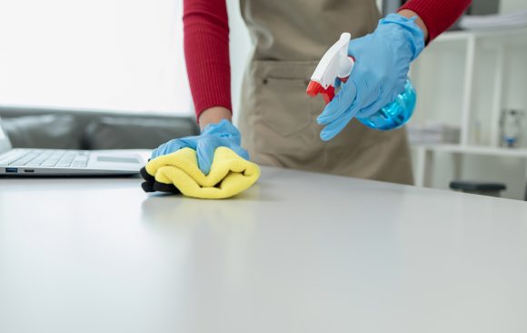 Cleaning desk surface in office with sanitizer spray, wear glove Declutter Before You Clean